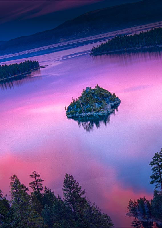 A view of an island on a lake glowing with a purple reflection of the sky.