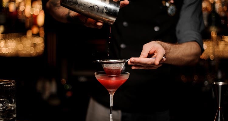 Bartender using shaker and sieve to make cocktail.