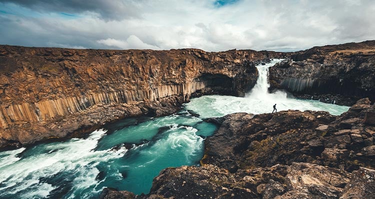 Rock fixtures with waterfall rushing through, person walking close to the waterfall.