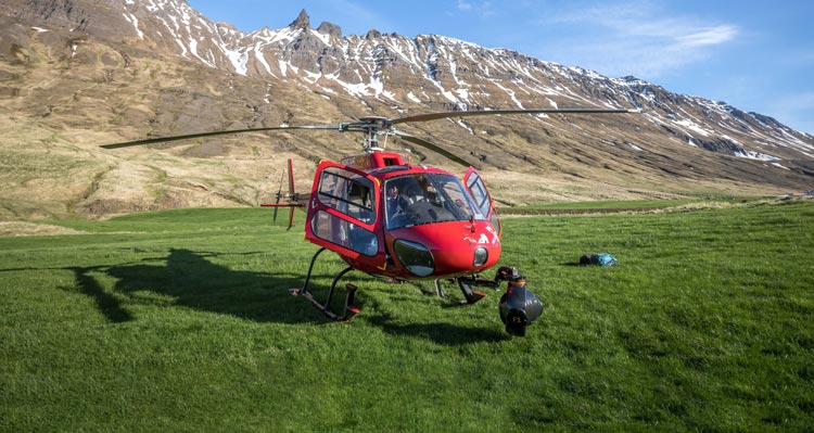 A helicopter on a green field below mountains.