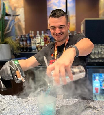 Blade Ohman, a bartender pours a blue drink into a smoky glass.